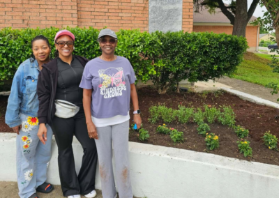 Three members in front of the church with freshly planted flowers.